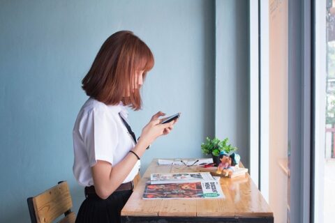 窓際で椅子に座ってスマートフォンを操作する女性